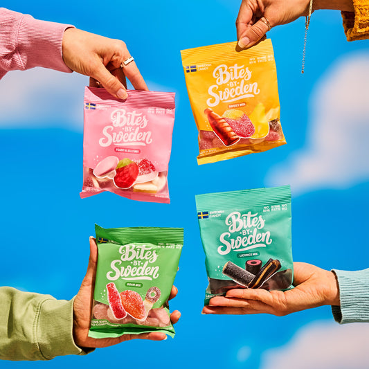 Four hands holding 'Bites of Sweden' snack packets against a blue sky.